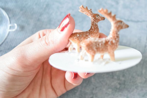 Abbi Kirsten's hand holds a cardstock circle with two miniature deer figurines glued on top. 