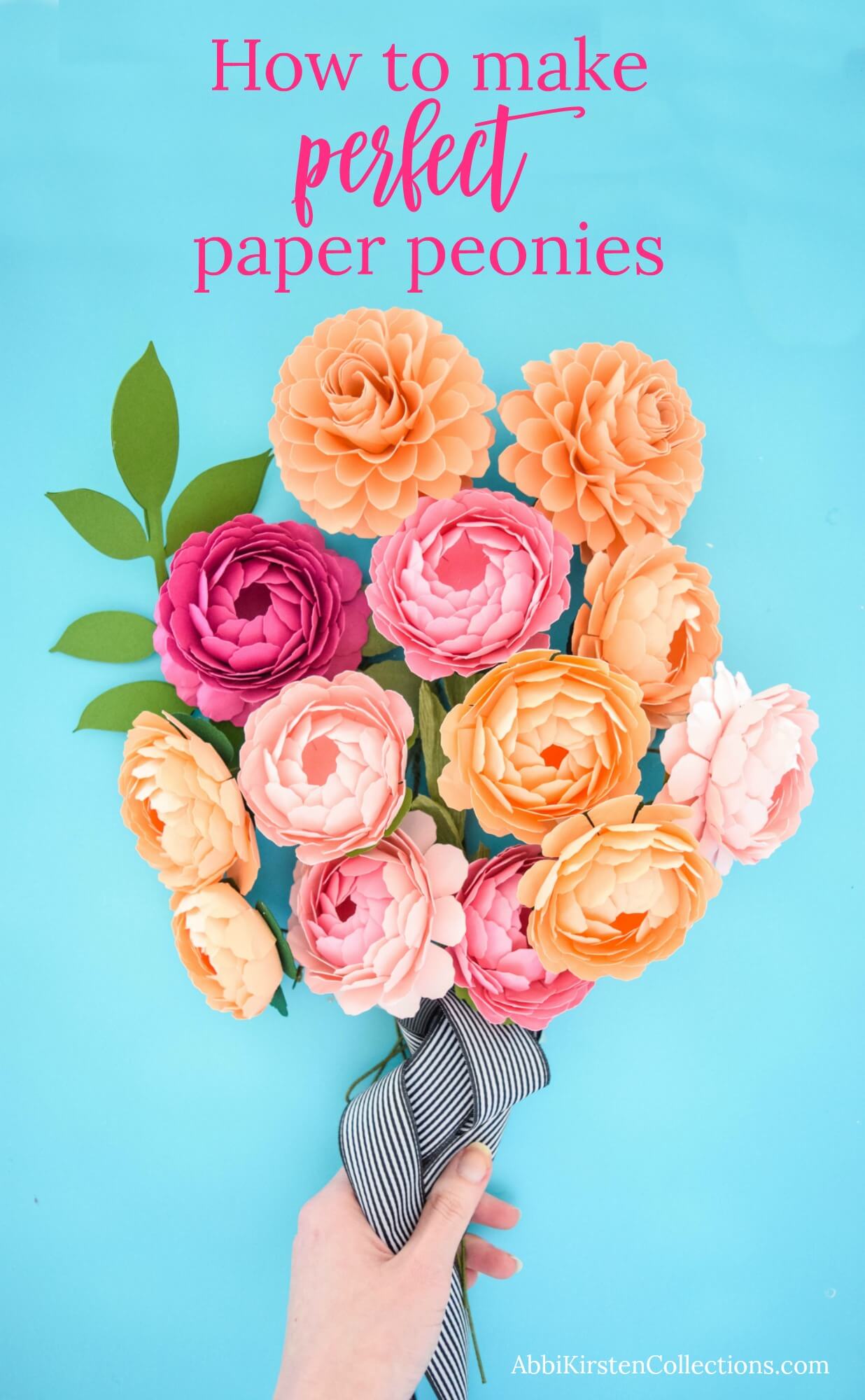 Abbi Kirsten's hand holds a bouquet of gorgeous paper peonies in red, pink, and orange. The flower stems are wrapped in a black-and-white striped ribbon. On the blue background are the words "How To Make Perfect Paper Peonies."