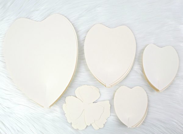 Five stacks of white paper petals are on a table ready to be made into a giant DIY paper Bella Rose flower. 