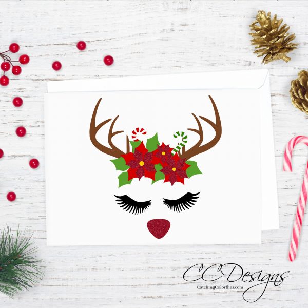 The free Reindeer Cut File & Poinsettia Template is the front of a Christmas card on a white wooden tabletop with a candy cane nearby. 
