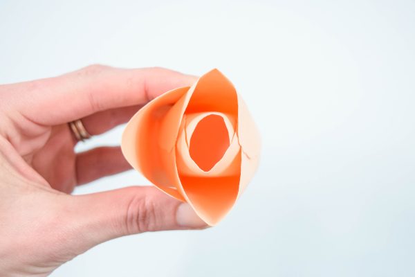 A woman's hand holds a paper rose center bud over a light blue background. 