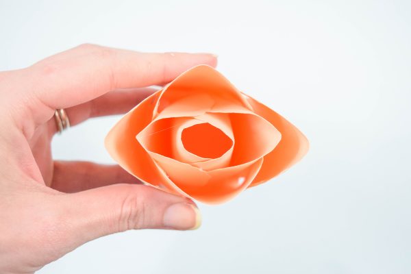 Abbi Kirsten holds a finished peach-colored serena paper rose center bud between her fingers and thumb.