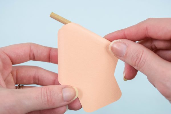 A paper rose petal is being curled by a thick wooden dowel held in Abbi Kirsten's hands.