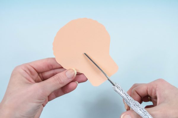 Two female hands use scissors on a large paper flower petal to cut a slit. 