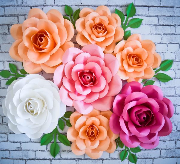 The DIY Paper Rose: Serena Rose is displayed on a gray brick background. The paper flowers are in shades of white, pink, and orange. 