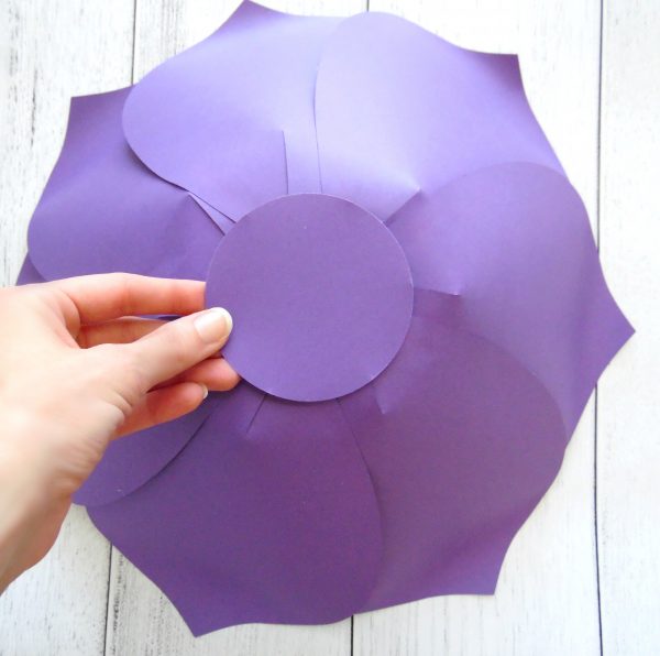 Abbi Kirsten places a circle of purple paper on the back of and outer layer of paper petals to create a base. 