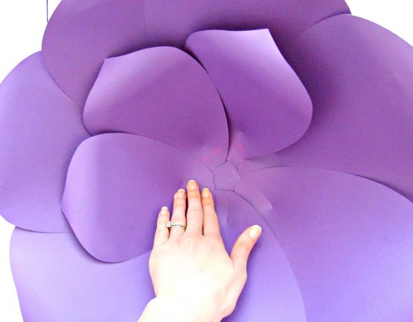 Abbi Kirsten's hand holds down the second layer of smaller purple paper petals that have been laid inside the outer layer of this giant paper flower. 