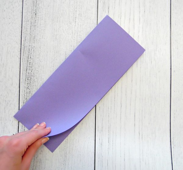 Abbi Kirsten folds a piece of purple paper in half lengthwise on a white wooden desk. 