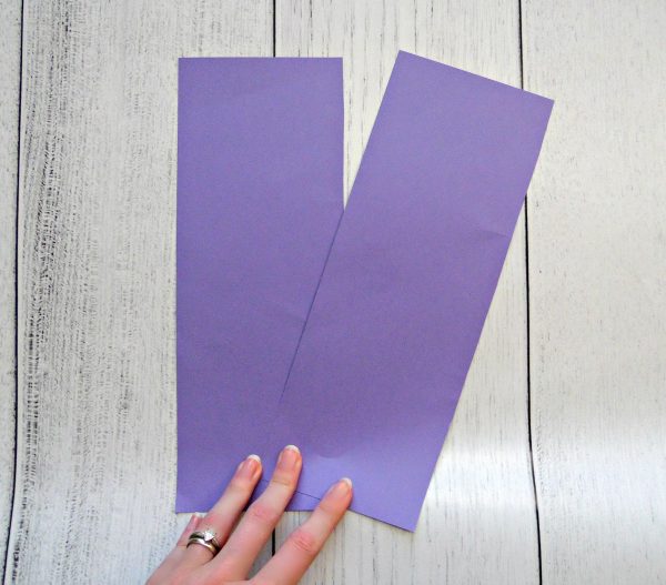 A look down at a white wooden desk. Abbi Kirsten displays two pieces of purple paper folded on the long-edge to use as a giant paper flower center. 