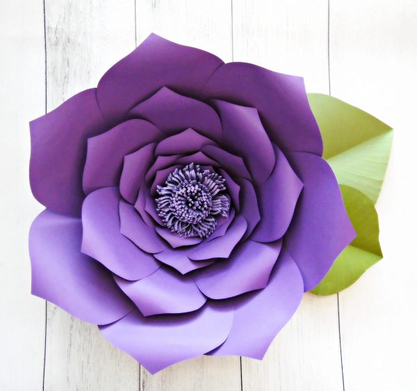 A giant purple paper flower with green leaves fills the frame. The petals are curled and a stamen center has been added which brings the paper craft deep dimensions. 