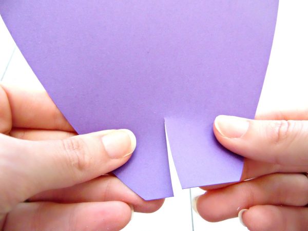 Abbi Kirsten holds the base of the purple paper petal demonstrating how to cross the petal ends over using the slit. This will create a cup that adds depth to your giant paper flowers. 