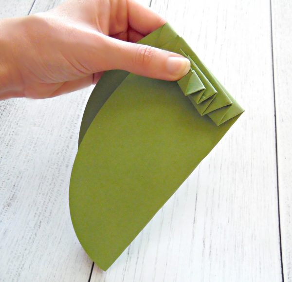 Abbi Kirsten's thumb holds down the multiple fold on the top of a giant green paper leaf. You can use this as a base for a giant paper flower. 