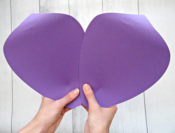 Abbi Kirsten holds two giant purple paper petals to use as the outer layer of a giant paper flower. The ends have been curled using a wooden dowel, which helps the paper flower look like it is blooming. 