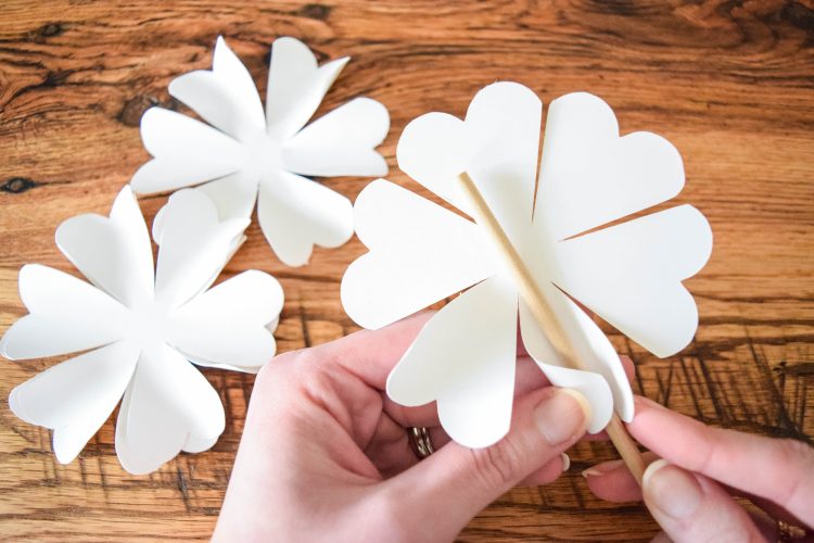 An image shows Abbi's hands using a thin wooden dowel to curl the edges of white paper flower petals.