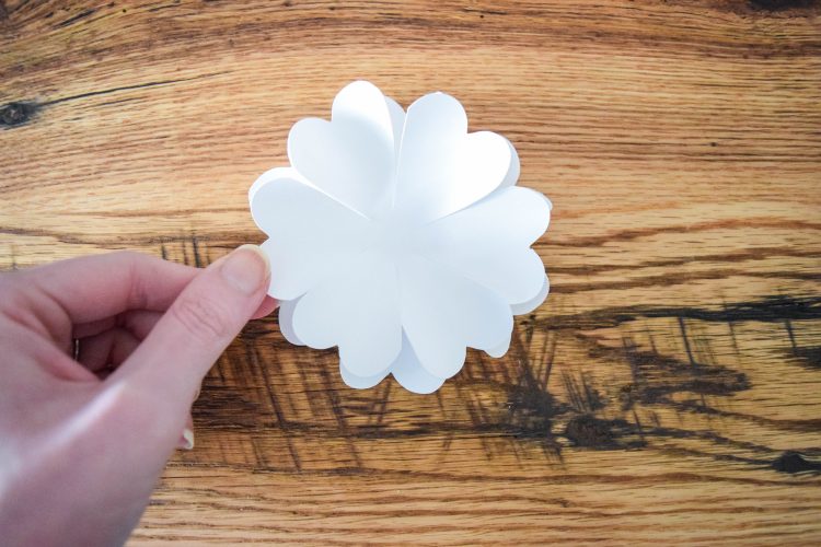 An image shows Abbi stacking layers of white paper flower petals - one of the first steps in creating white pomander flower ball.
