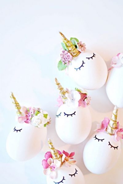 Six unicorn easter eggs with gold horns laying on a white table. 