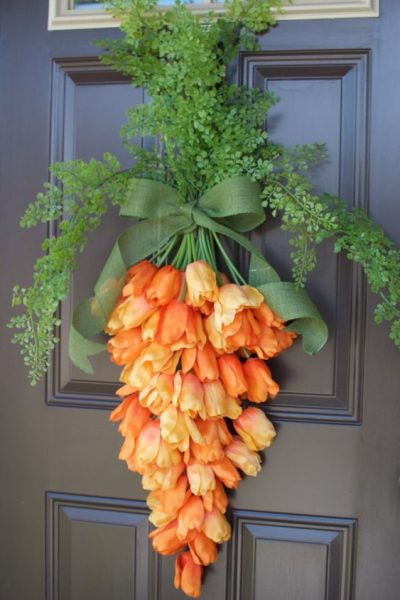 Orange roses hanging upside with green foliage on top and tied with a green ribbon hanging on a door. 