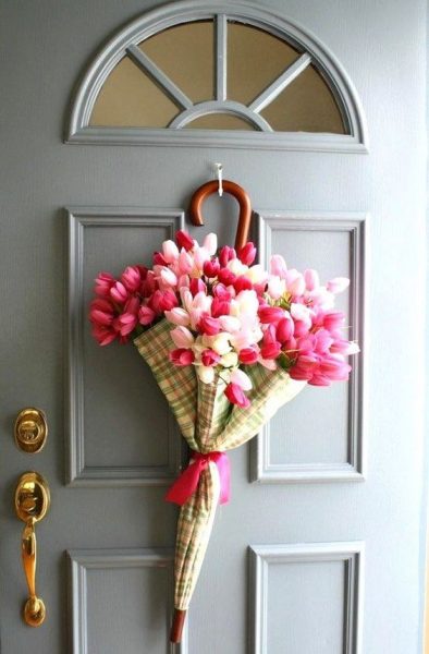 A yellow, green and orange plaid umbrella filled with pink and white tulips hanging on a grey door. 