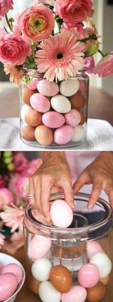 A large clear vase filled with pastel eggs and pink flowers. 