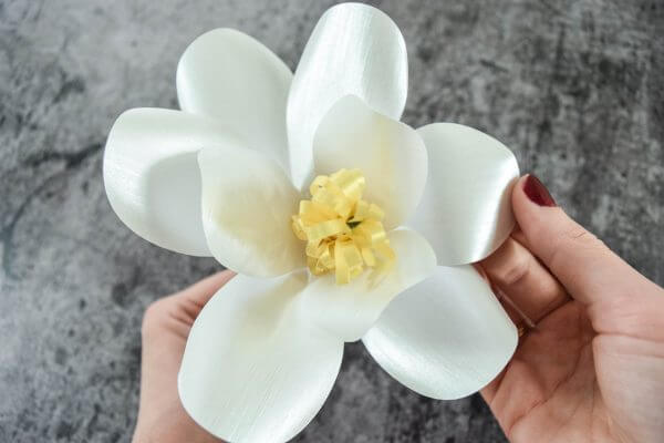 A white Magnolia Paper Flower with several shiny white petals and a yellow center.