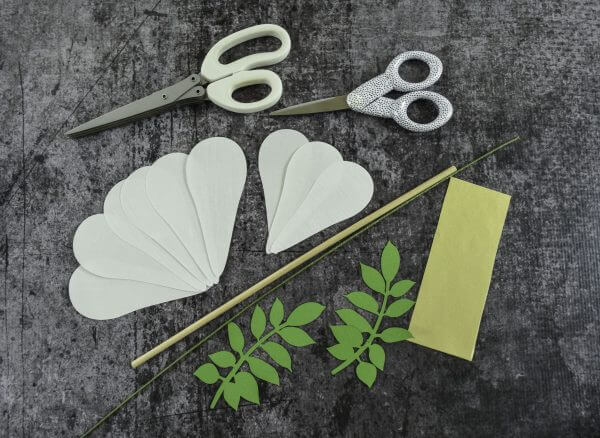 The supplies needed to make Magnolia Paper Flowers - scissors, white flower petals, leaves, and floral wire for the stems.