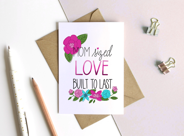 A white card that reads "mom sized love built to last". Bright flowers surround the text. The card lays on top of a brown envelope.