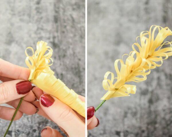 A woman's fingers wrap yellow fringed paper around the end of from floral wire.