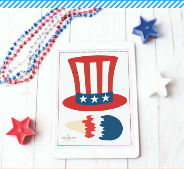 A white tablet with an image of a Fourth of July top hat and a red, white and blue ice cream cone. The tablet is sitting on a white wooden table decorated with red, white and blue candles and star necklace. 
