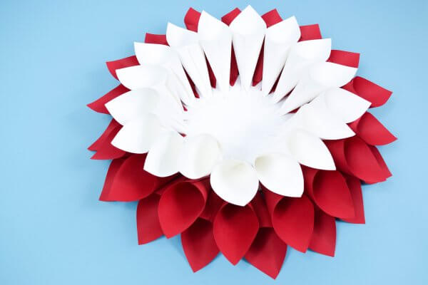 A layer of white paper cones sits on top of a double layer of red paper cones, creating a growing 3D effect.