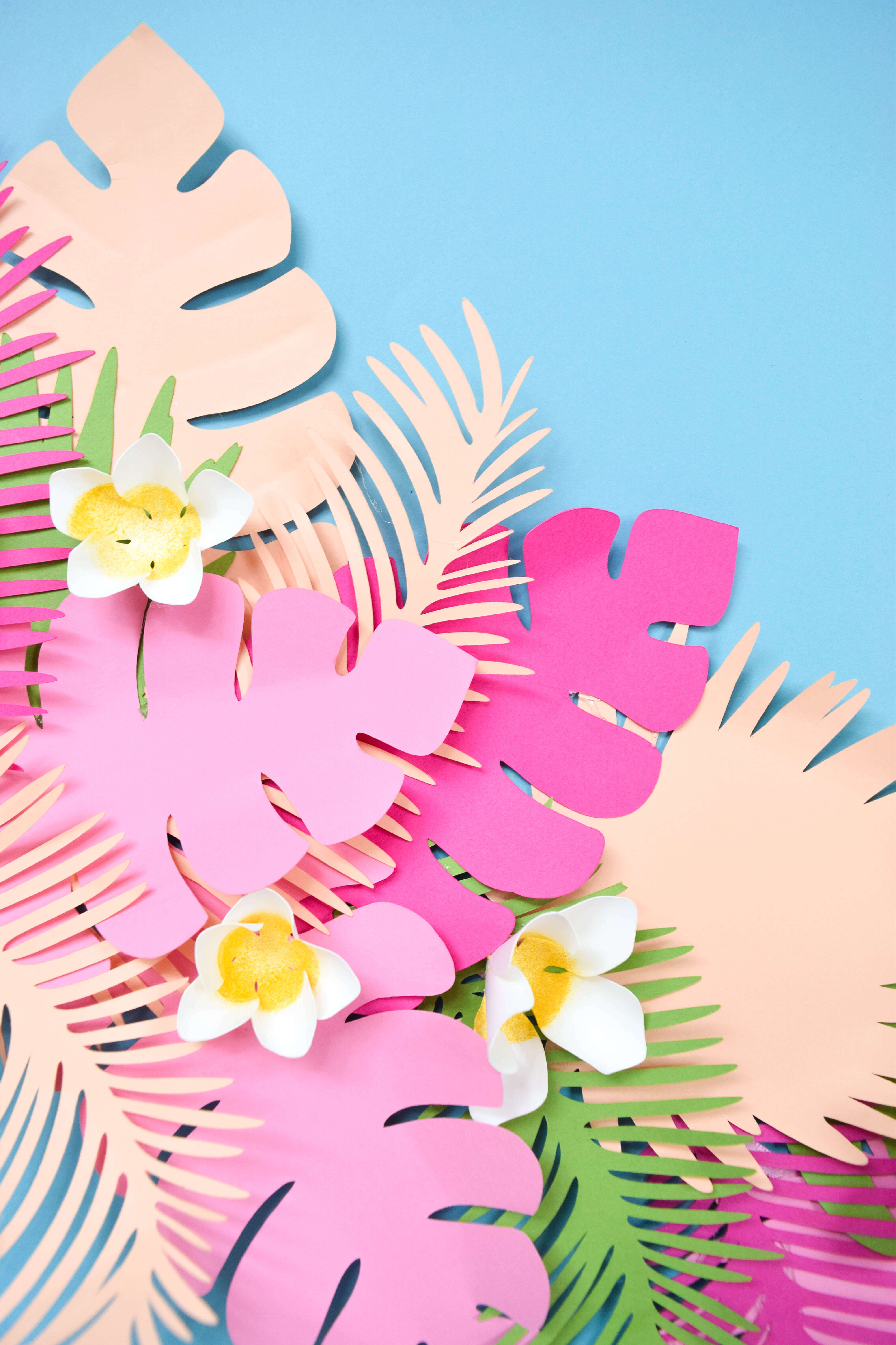 Tropical style paper leaves are cut out of pieces of cardstock. The giant paper leaves are cut from pink, coral, and green paper.