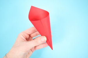 A woman holds a piece of red paper curled into a cone-shape in front of a bright blue background.