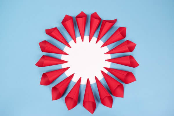 A circle of red paper cones arranged around a white paper circle in the center, laid out on a bright blue background.