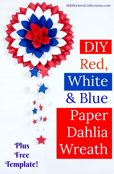 A patriotic paper dahlia flower wreath hangs on a white wall. Text overlayed onto the image says "DIY red, white, and blue paper dahlia wreath" in white text.