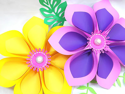 An overhead view of giant, colorful Hawaiian paper flowers and leaves on a white background. Abbi Kirsten designed these flowers, which are great decorations for photo backdrops and backyard BBQs. 