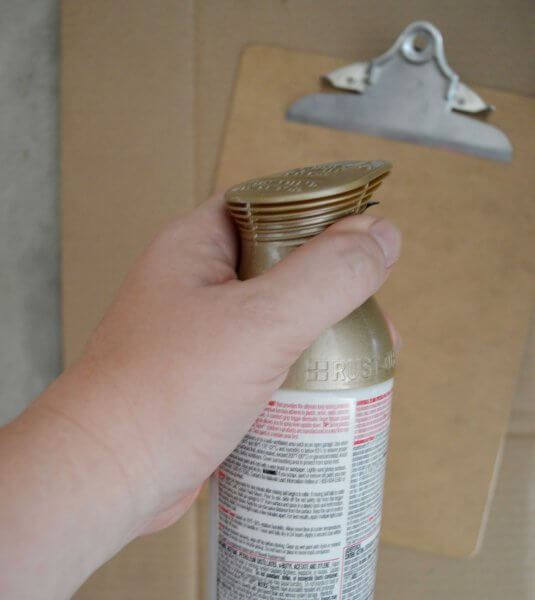 A woman's hand holds the top of a spray can, ready to paint the clipboard below. 