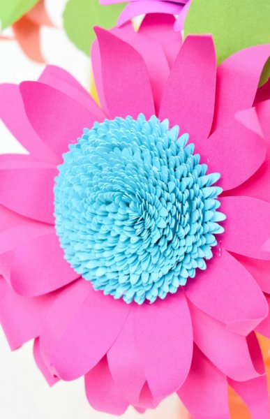 A close-up image of a pink paper sunflower with a bright blue center.