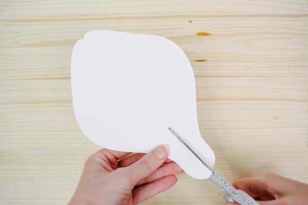 Scissors cutting a slit into a giant white paper petal. 