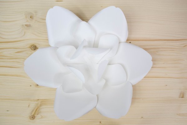 A third layer of curled white paper petals attached to two layers of larger white paper petals on a wooden table. 