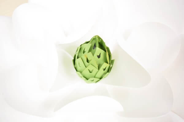 A close-up image of a giant white paper magnolia flower with a light green center. 