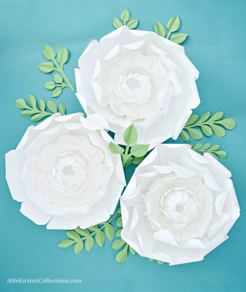 Three completed giant snowy paper peony flowers. From overhead you can see the cupped center petals and the paper greenery underneath the flowers.