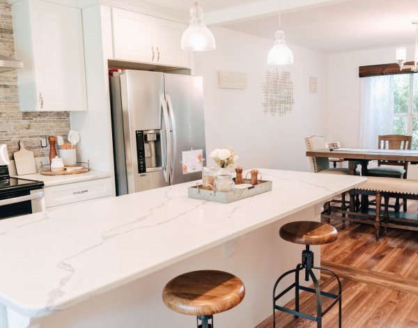 An angled view from one side of the kitchen island to include a view of the renovated dining room. Both rooms are clean and cozy, and designed in creams and whites. 