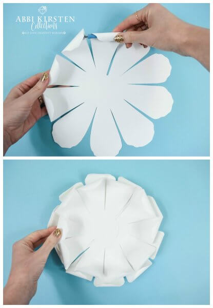 Abbi Kirsten's hands curl the petals of the white petals inward to make the paper flower more realistic. A second image shows the inner curled petals stacked on top of each other. 