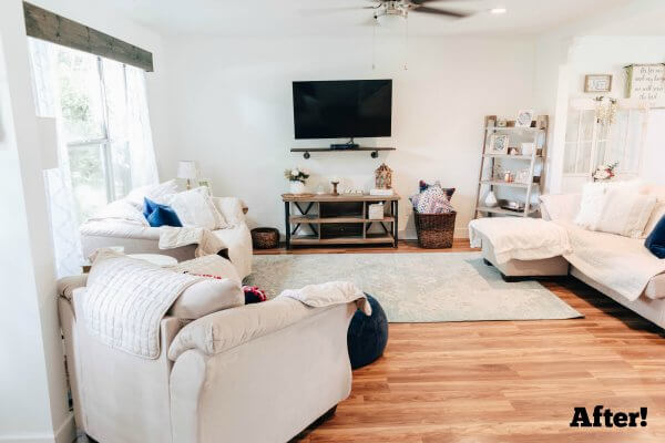 A full family room, full of white furniture, curtains, and rugs is merged with a living room. A TV hangs on the far wall while a large window occupies the left wall. The room looks clean, cozy, and open. Typed in the right corner is the word "After!"