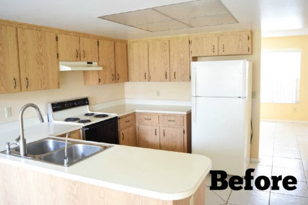 A sad outdated kitchen in a U-shape, with beige cabinets and walls, and a vinyl tile floor. In the corner is the word "Before."