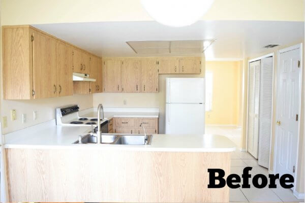 A small outdated beige kitchen in a U-shape. White doors line one wall of this empty kitchen. "Before" is written in the bottom right corner. 