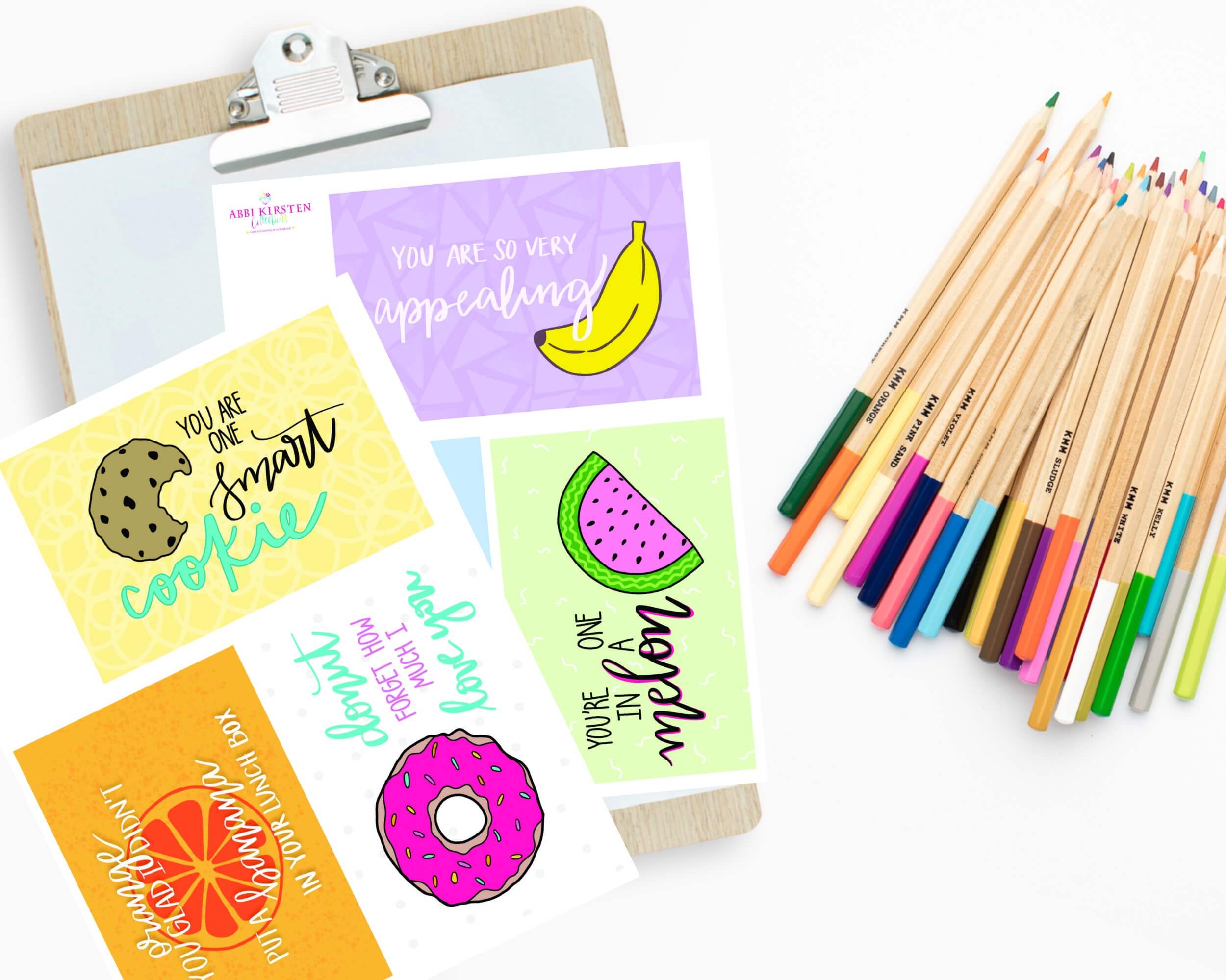 Colorful back-to-school lunch box printables lay next to a bundle of colored pencils. Phrases include "You are one smart cookie" and "You're one in a melon.”