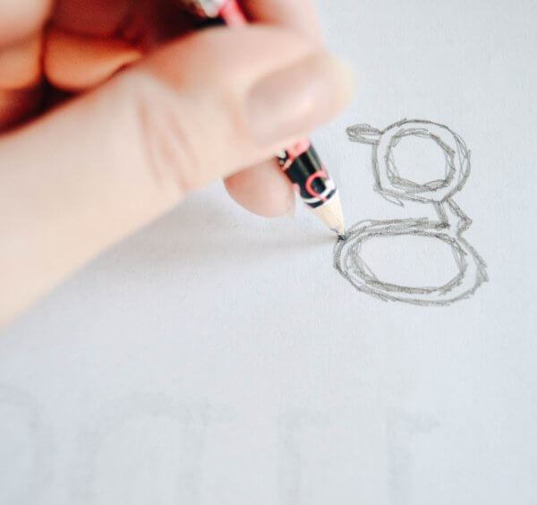 A hand holding a pencil drawing the lowercase letter "g" onto white paper. 