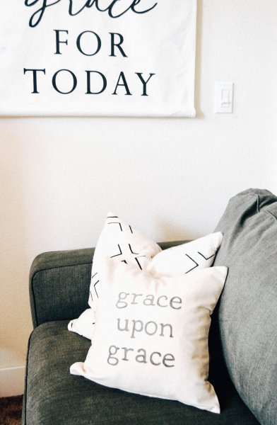 Two pillows, one with text that reads "grace upon grace", set on a grey couch. 