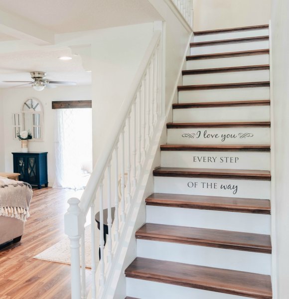 The open concept family and living room combo carries through a creamy color scheme. The staircase on the right has been stripped of carpet and is white and dark wood. The stairway reads "I love you every step of the way" in craft vinyl made using SVG cut files and Abbi Kirsten's Cricut machine. 