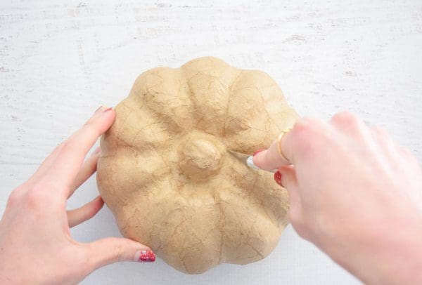 Abbi carefully uses an Exacto knife to cut the paper mache pumpkin stem off, making a hole in the top of the craft pumpkin.